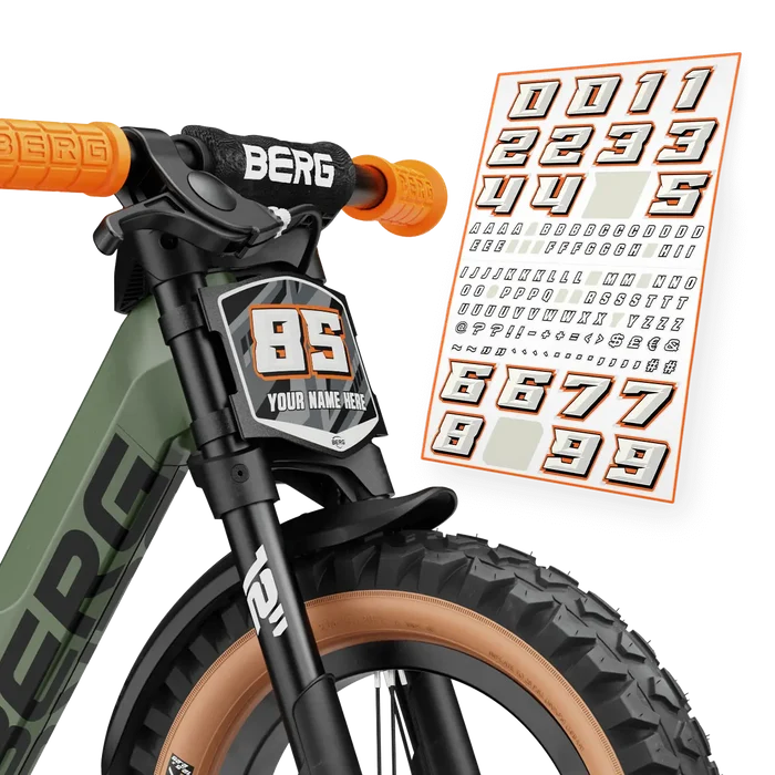 Front of a green balance bike with orange grips, knobby tires, and a customizable number plate sticker kit.