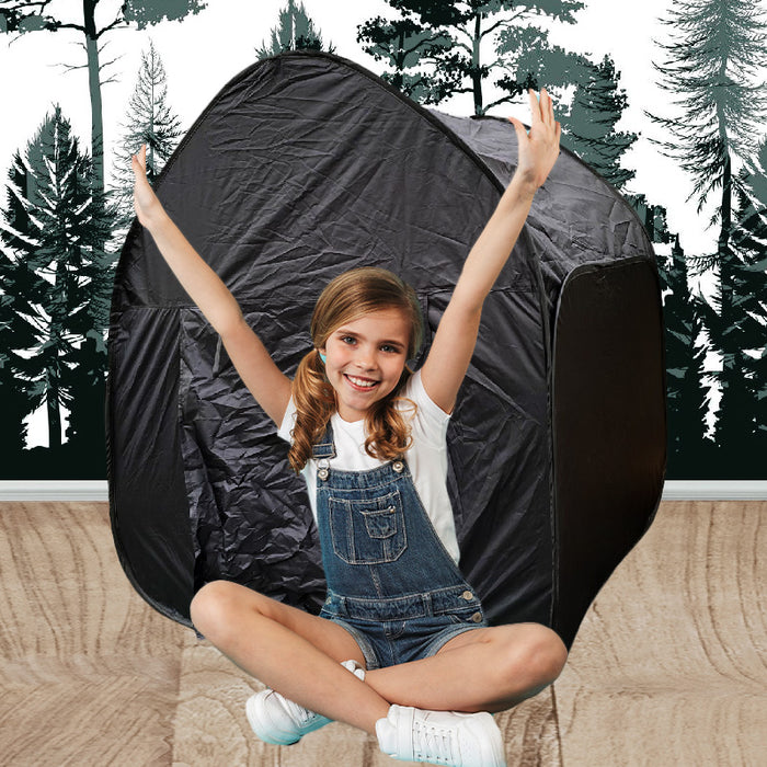 A happy girl sits with arms raised in front of a dark, rounded pop-up tent against a forest-themed background.