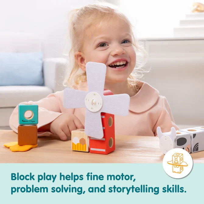Smiling toddler girl plays with a wooden windmill and animal-themed building blocks on a table.