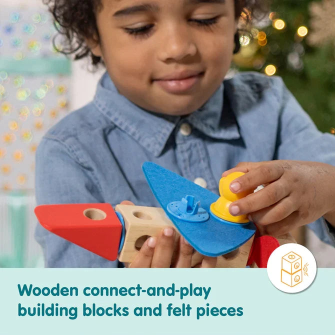 Child assembling a toy with wooden blocks, a red plastic nose, blue felt wings, and a yellow connector piece.