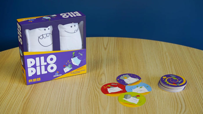 Purple Pilo Pilo game box with white plush pillows and round illustrated cards on a light wood table.