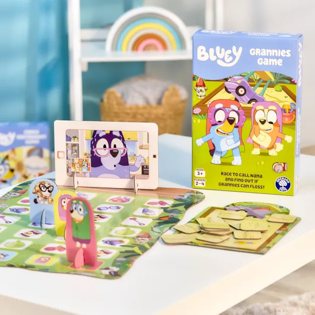 Bluey Grannies board game with character standees and cardboard tablet set up on a white table next to its box.