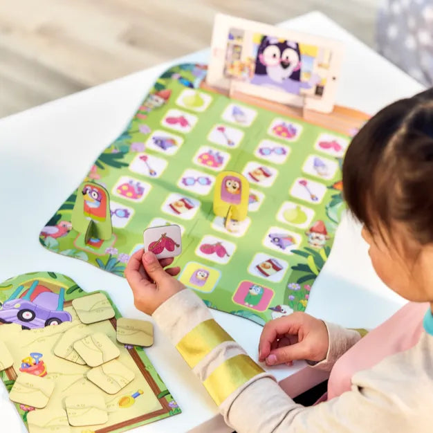 Child plays Bluey Grannies game with character standees and colorful matching tiles on a green illustrated board.