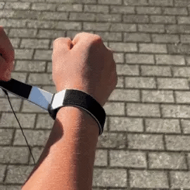 Person tightening a black and white Velcro wrist strap with an attached thin black cord over a grey brick walkway.