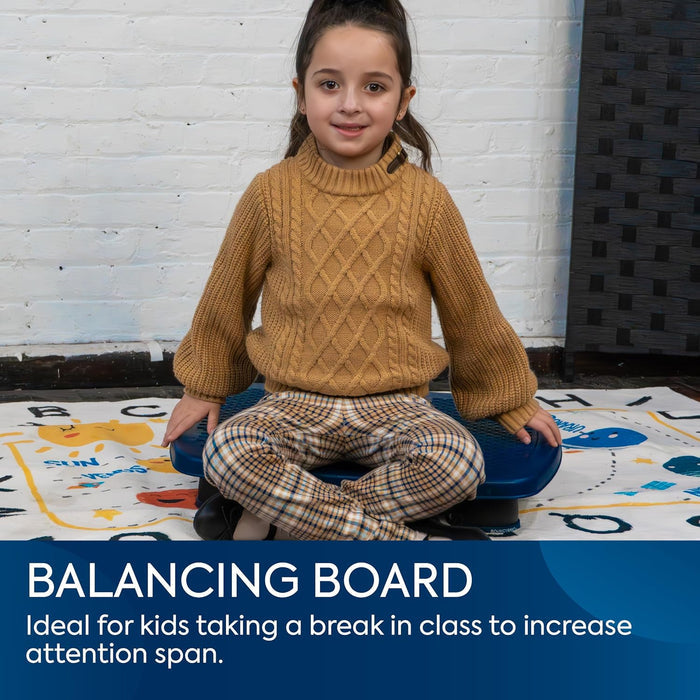 A young girl sits cross-legged on a blue plastic balance board over a colorful mat with a white brick wall background.
