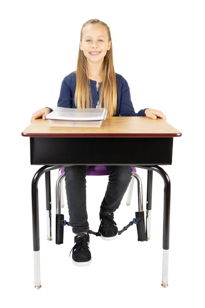 A child at a desk rests her feet on a black elastic band stretched across the front legs of her purple chair.