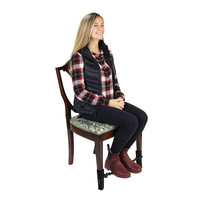 Woman sitting on a wooden chair with her feet resting on a black elastic band stretched between the front legs.