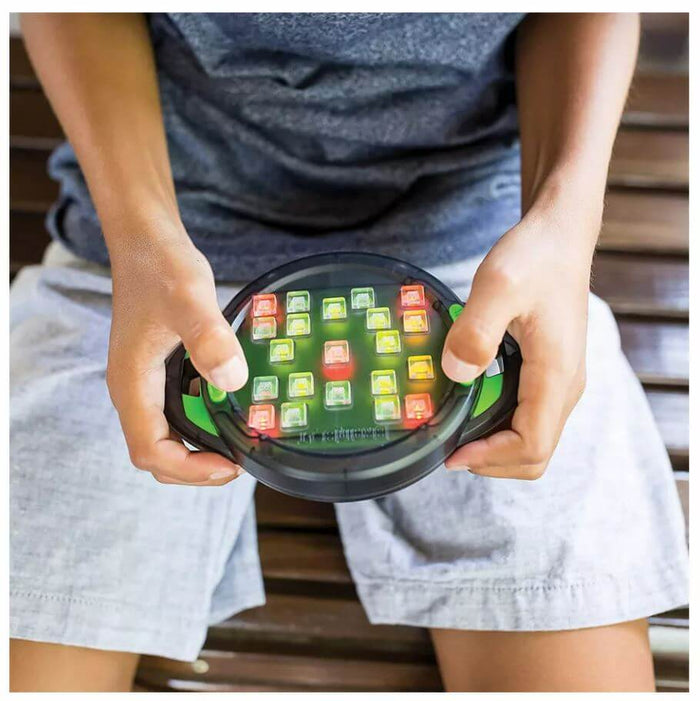Hands holding a round black handheld game with a grid of light-up red, yellow, and green square buttons.