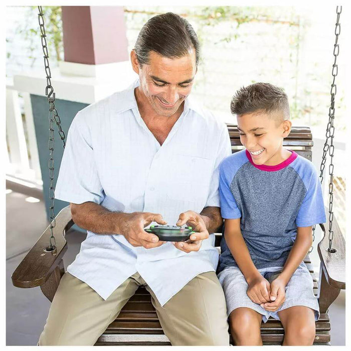 Man and boy smiling on a porch swing while playing with a small, circular black electronic game with green buttons.