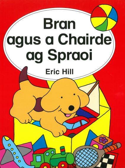 Yellow puppy in a toy box with colorful toys like a train and ball on a red children's book cover with Irish text.