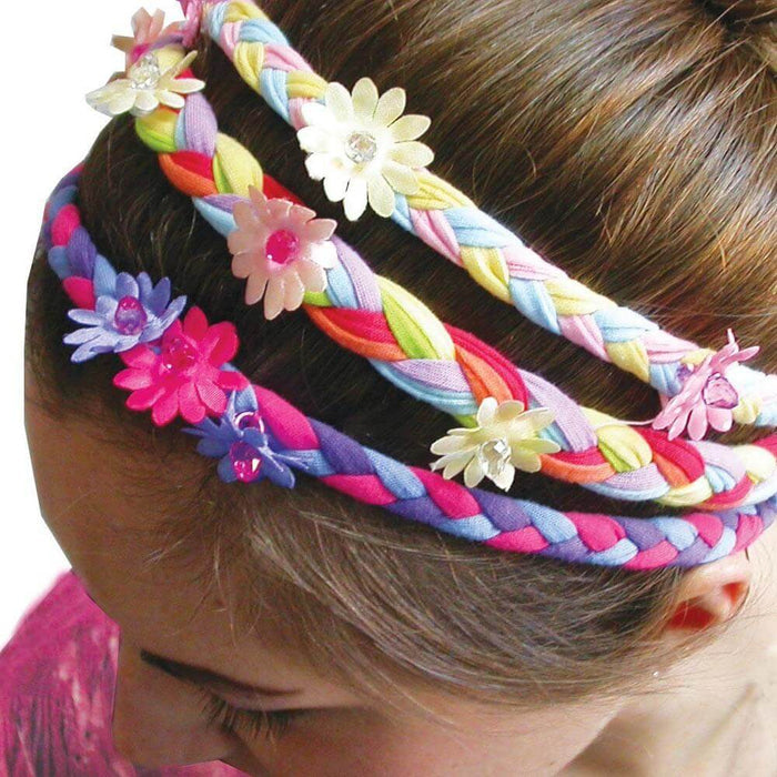 Three multi-colored braided headbands with small jewel-centered flowers worn on a girl's brown hair.