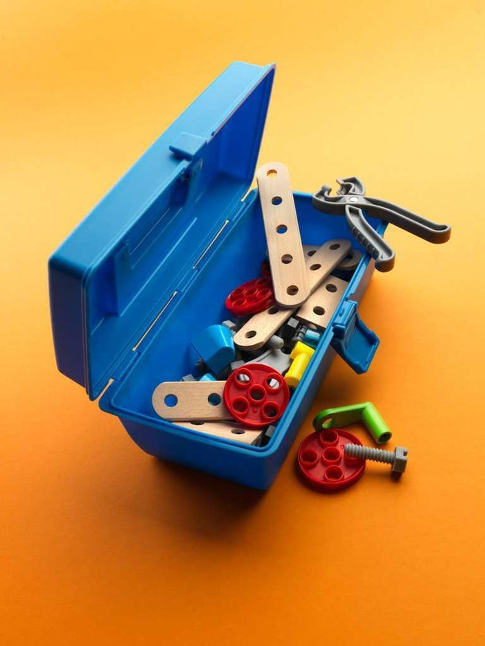 Open blue toolbox with wooden planks, red wheels, grey pliers, and colorful building pieces on an orange background.
