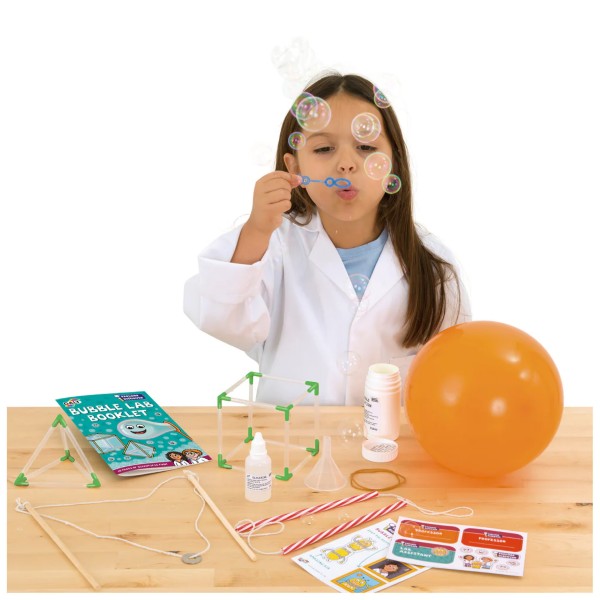 Child in white lab coat blowing bubbles with kit including orange balloon, 3D wire frames, and instruction booklet.
