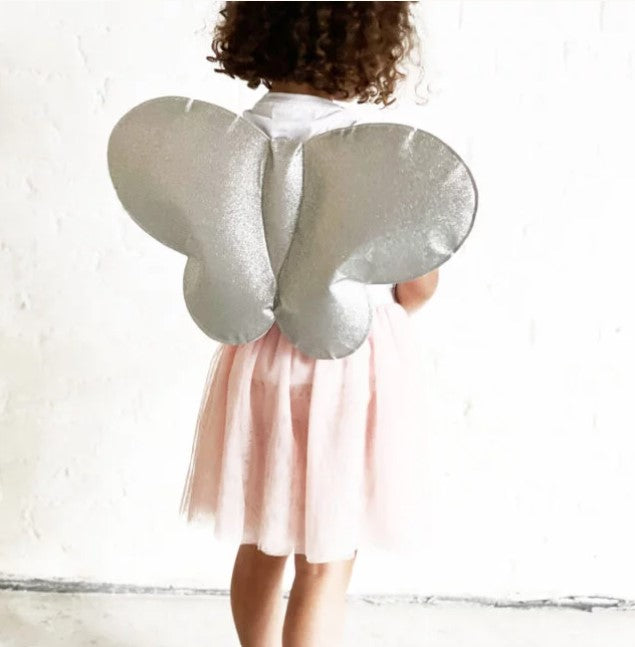 A young girl from behind wears shimmering silver butterfly wings and a pale pink tulle tutu skirt.