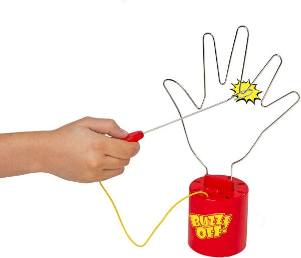 Hand holds a metal wand looped around a wire hand frame on a red base. A yellow spark shows a buzzer touch.