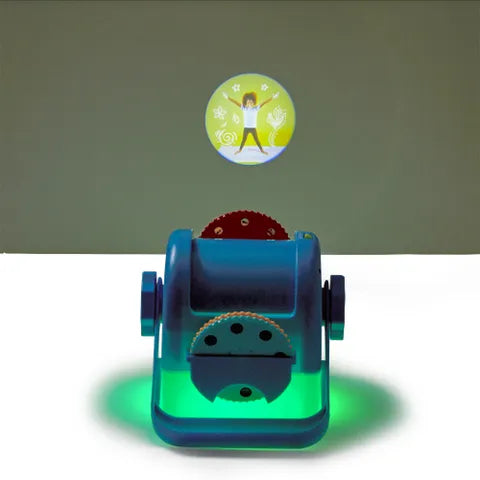 A blue toy projector glowing green, projecting a circular image of a person in a yoga pose onto a dark wall.