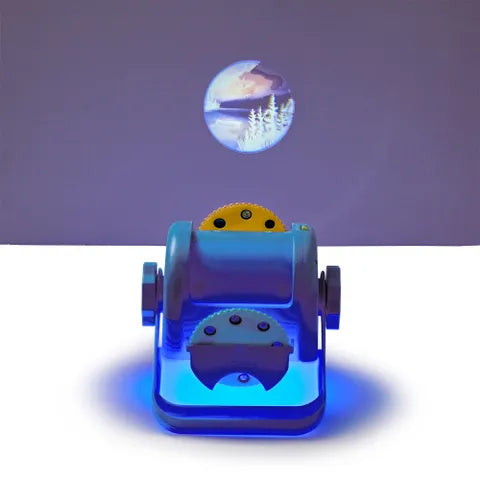 Blue projector toy with yellow gears casting a circular winter forest scene onto a purple wall.