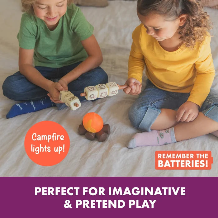 Two children play with a glowing orange campfire toy and marshmallow blocks with story icons on roasting sticks.
