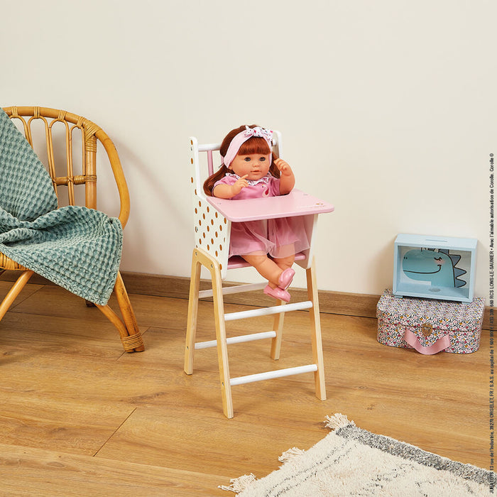 Wooden doll high chair with a pink tray and gold-dotted white seat, shown with a doll sitting inside.