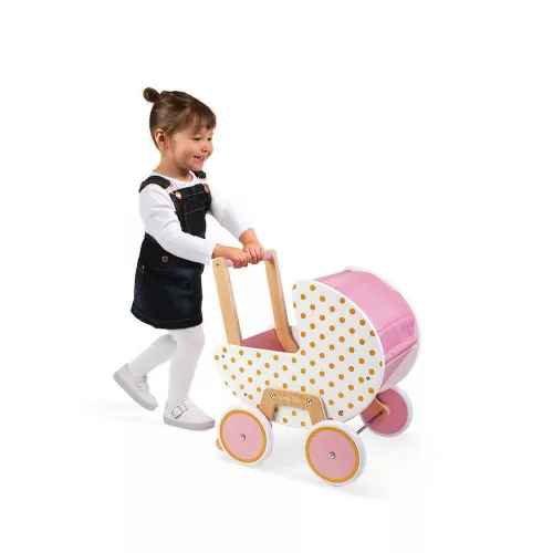 Young girl pushes a white wooden doll pram with gold polka dots, pink fabric hood, and pink wheels.