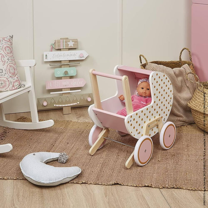 White wooden doll pram with gold polka dots, pink interior, and natural wood frame, shown in a cozy nursery.