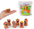 12 tiny brown capybara squishies with colorful hats in a clear tub, shown in a hand to demonstrate miniature size.
