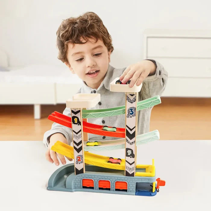 Young boy playing with a 4-tier wooden car ramp toy featuring colorful tracks, toy cars, and a grey garage base.