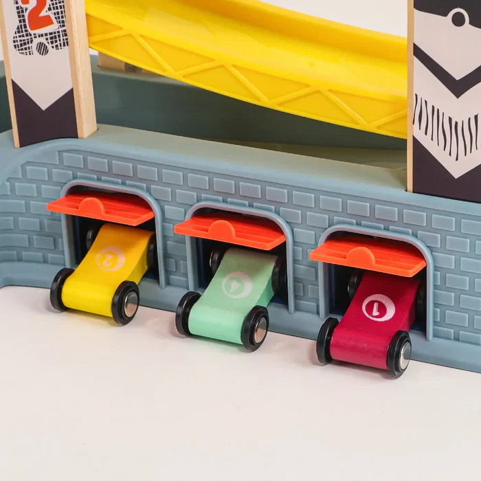 Three numbered toy cars in yellow, green, and red emerging from orange garage doors beneath a yellow track ramp.