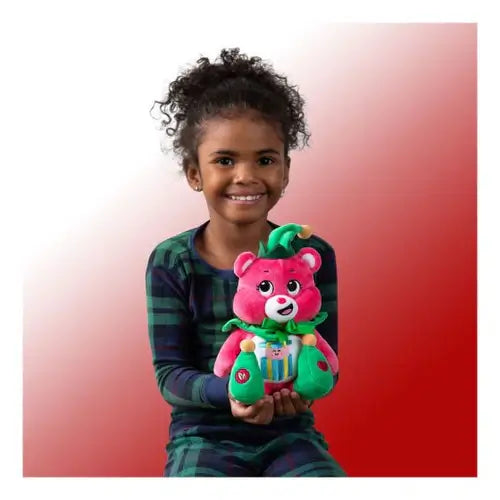 Young girl holding a pink Care Bear elf plush with a green hat and collar, wearing green plaid pajamas.