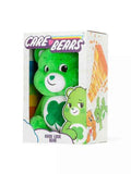 Bright green plush Good Luck Bear with a clover belly, packaged in a white Care Bears window box with character art.