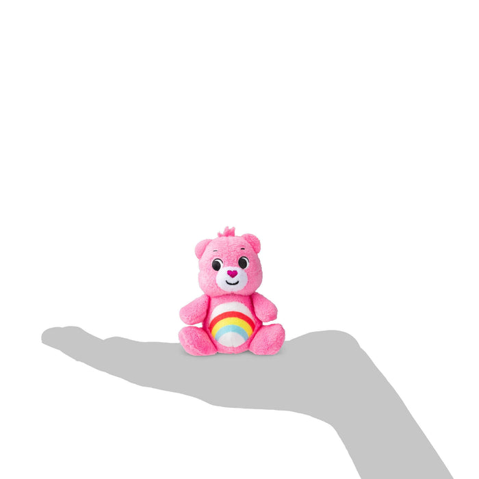 Small pink Care Bear with a rainbow belly sitting on a grey hand silhouette to show its micro scale.