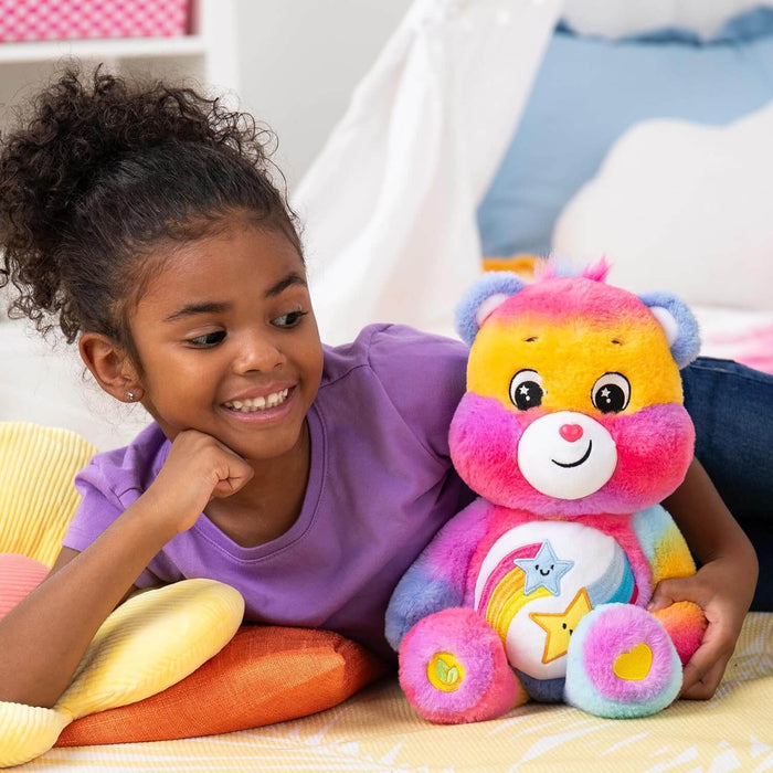 A young girl smiles at a colorful tie-dye Care Bear plush with a star and rainbow badge on its white belly.