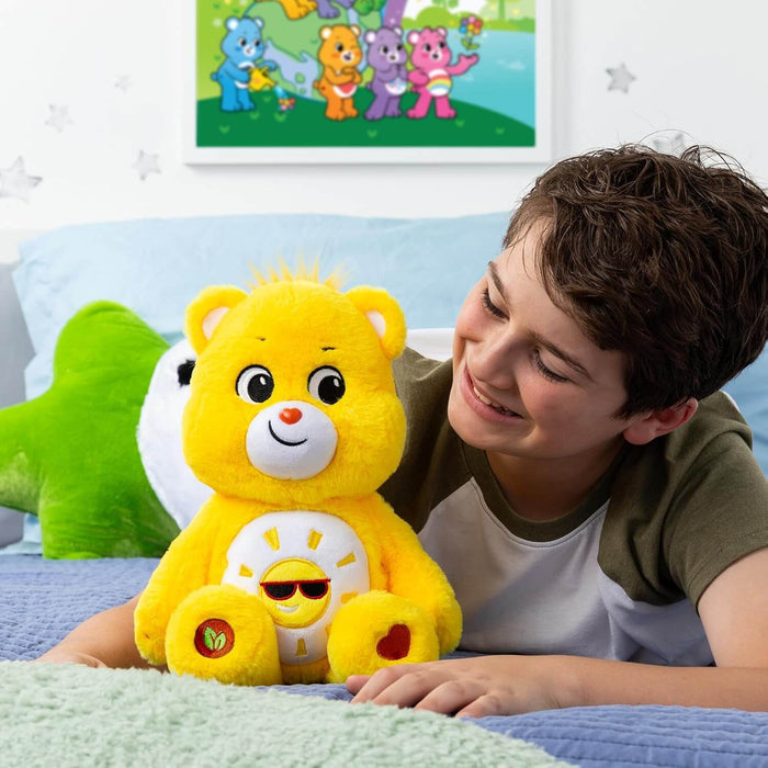 Bright yellow plush bear with a smiling sun in sunglasses on its belly, sitting on a bed next to a child.