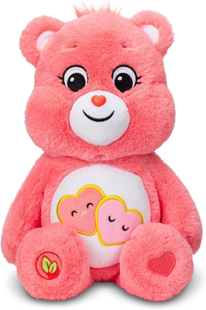 Coral pink plush bear with two smiling hearts on its white belly and a red heart on its foot, sitting front-facing.