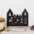 Matte black castle-shaped wall chalkboard decorated with colorful magnet shapes in a modern playroom.