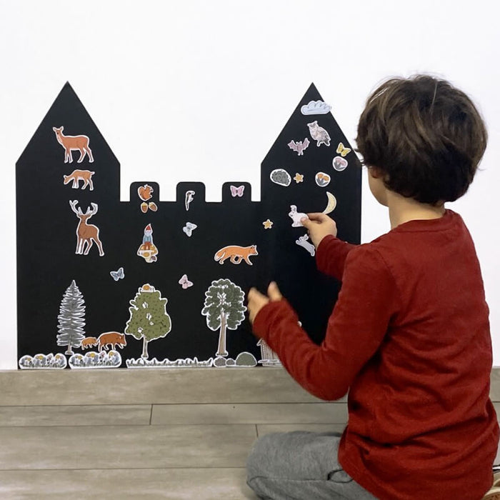 Child in a red shirt placing animal magnets on a black castle-shaped magnetic chalkboard.