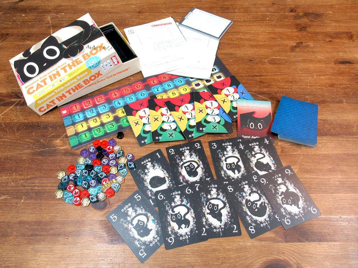 Cat in the Box board game packaging, black cat-themed cards, colorful tokens, and a numbered board on a wooden table.