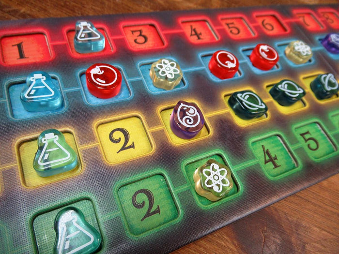 Close-up of a dual-layered game board with colorful acrylic tokens featuring beaker, atom, and planet icons.