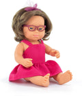 Caucasian baby doll with Down syndrome features, purple glasses, brown hair with a bow, and a bright pink dress.