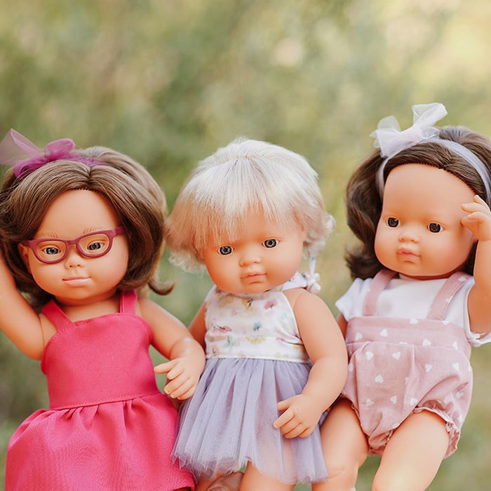 Three baby dolls with Down Syndrome features; the left doll wears purple glasses and a bright pink dress.