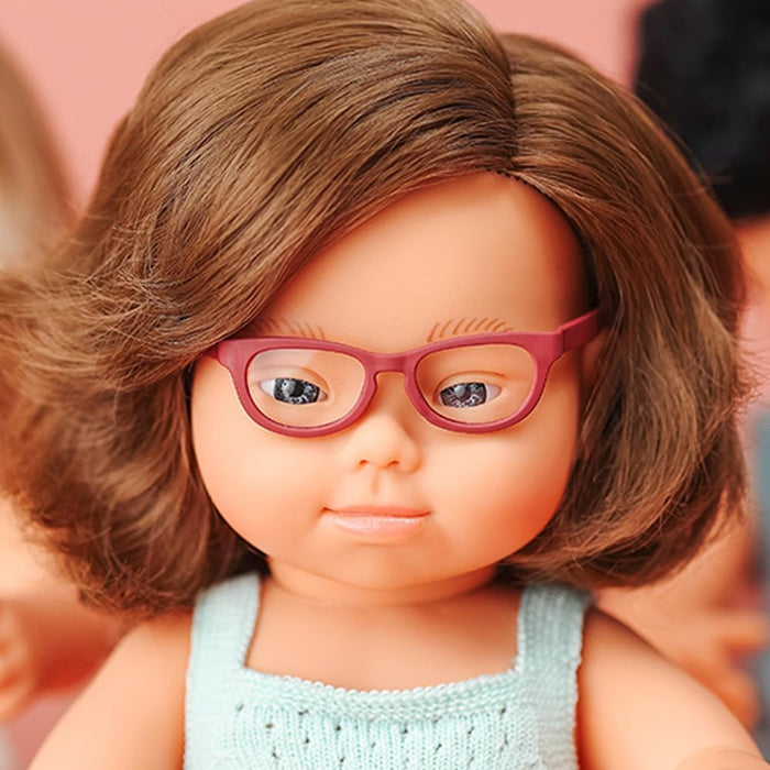 Baby doll with Down syndrome features, wavy brown hair, pink glasses, and a light blue knitted top.