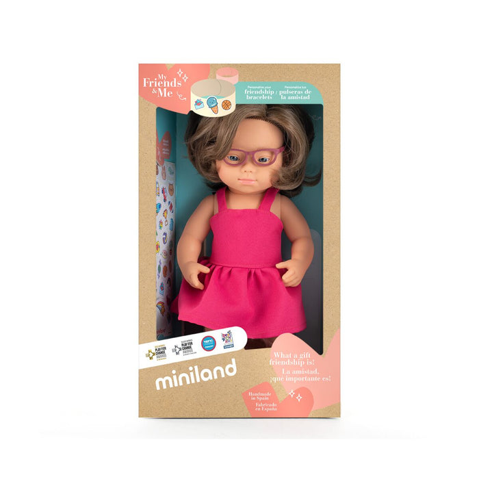 Brown-haired doll with Down syndrome features wearing pink glasses and a pink dress in a cardboard window box.