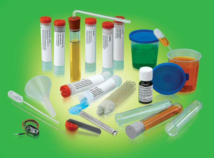 Labeled test tubes with colorful liquids, powders, beakers, and science tools arranged on a vibrant green background.