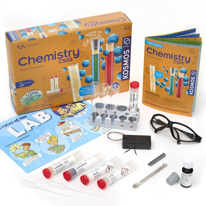 Kosmos Chemistry C500 kit with orange box, instruction manual, test tubes in rack, safety goggles, and chemical vials.