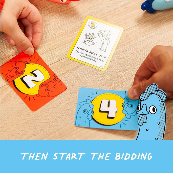 Hands hold orange hotdog and blue chicken numbered cards next to a yellow flip challenge card on a wood table.