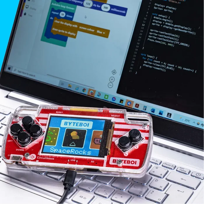 Red and white DIY handheld console in a clear case on a laptop showing block and text-based coding software.