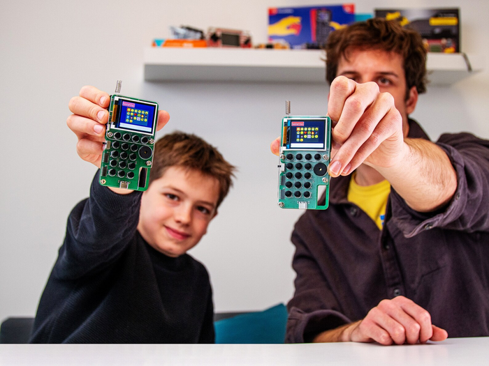 Adult and child holding green circuit board walkie talkies with color screens, antennas, and black buttons.