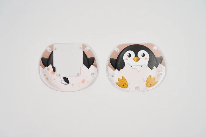 Two semi-circular plastic pieces featuring a cartoon penguin hatching from a white egg with yellow feet.
