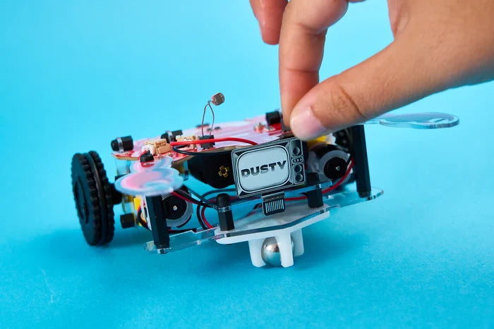Hand adjusting a DIY robot with a clear chassis and DUSTY screen on a bright blue background.