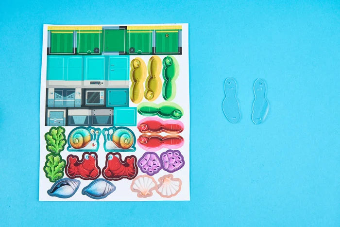 Sticker sheet featuring crabs, snails, and seashells next to two clear plastic pieces on a light blue surface.